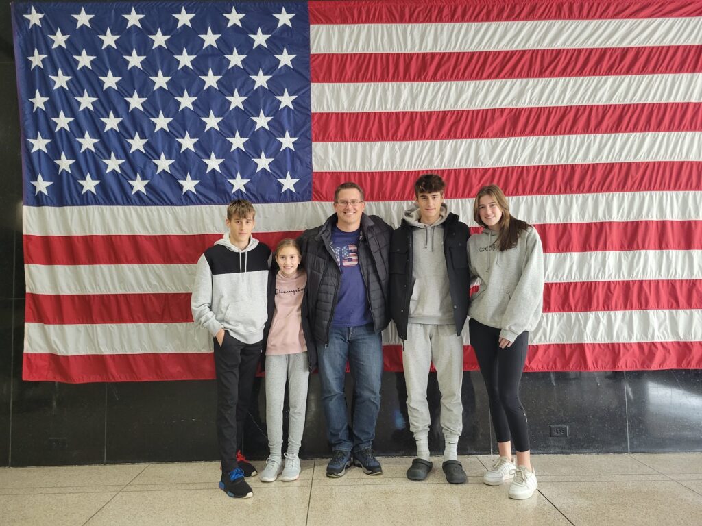 Grim family stands in front of an American flag on the day they became U.S. citizens