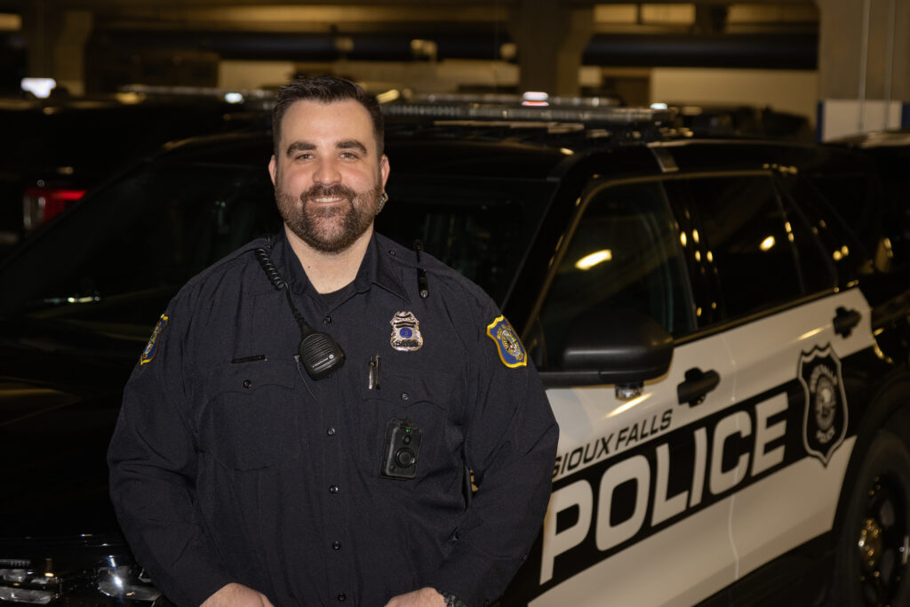 SFPD Officer Garrett McCarthy stands in front of a Sioux Falls police cruiser